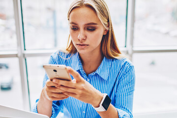 Wall Mural - Serious female entrepreneur checking email box on smartphone texting feedback while spending time in office,businesswoman using application on smartphone for banking online making transaction