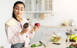 © Prostock-studio - Healthy vs Unhealthy Food. Decisive doubtful woman holding red apple and donut in both hands, making choice of her meal, standing in kitchen, free copy space. Uncertain lady hesitating about her diet