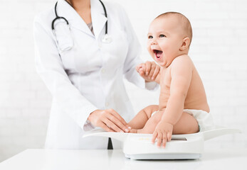 weight measuring. adorable little baby sitting on scales , medical check up with female pediatrician