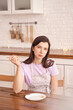 © elenavolf - Pensive woman in apron holding chopsticks in minimalist kitchen with string lights and brick wall.