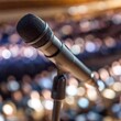 © LIGHTFIELD STUDIOS - A high-resolution ultrarealistic image featuring a detailed digital photograph of a microphone on a stand placed center stage in a large, packed auditorium. The microphone has a golden body with a bla