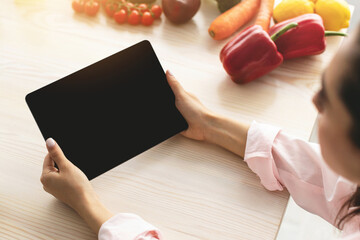 Aufkleber - Over the shoulder view of young woman holding and using digital tablet with black empty screen for mock up template, cooking in kitchen, drinking coffee in the morning, searching new recipes online