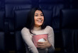 © Prostock-studio - Going to movies alone concept. Lovely Asian woman with popcorn enjoying film in cinema