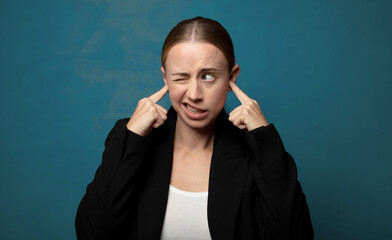 Wall Mural - looking angry, stressed and annoyed, covering both ears to a deafening noise, sound or loud music