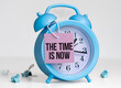 © Pawel - Blue alarm clock with text on card The Time is Now on white background.