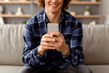 Poster - Unrecognizable Hipster Guy Using Mobile Phone Texting And Browsing Internet, Networking In Social Media Online Sitting On Sofa Holding Smartphone At Home. Man With Cellphone Using Application. Cropped