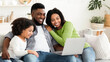 © Prostock-studio - Family Weekend. Cheerful black parents and their little daughter using laptop at home together, watching movie or browsing internet, free space