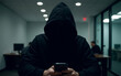 © leesle - A faceless man in a black hooded jacket holds a phone in his hands against the background of an office. Concept of fighting against telephone scammers hackers. Low key, dramatic light.
