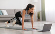 © Prostock-studio - Active young brunette woman in sportswear exercising at home in front of laptop, watching fitness video on Internet or having online fitness class, cozy living room interior, copy space