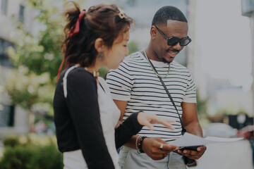 Wall Mural - Two professionals engage in a casual business discussion outdoors, sharing documents on a bright day. They appear focused and collaborate efficiently, exemplifying teamwork and communication in a