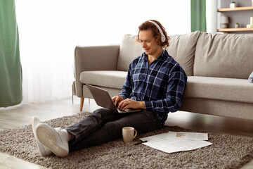 Poster - Happy Man Working On Laptop Wearing Headphones Browsing Internet Sitting On Floor At Home. Freelancer Guy Using Computer In Living Room. Distant Job, Internet And Technology