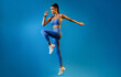 © Prostock-studio - Female Athlete Jumping Exercising During Training Over Blue Studio Background, Looking Aside. Fitness Workout And Sport Motivation Concept. Full Length, Side View