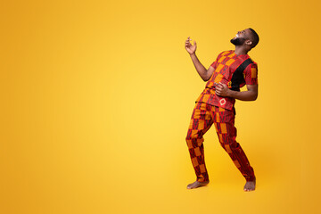 Wall Mural - Joyful african american young man fooling over yellow background, playing on imaginary guitar