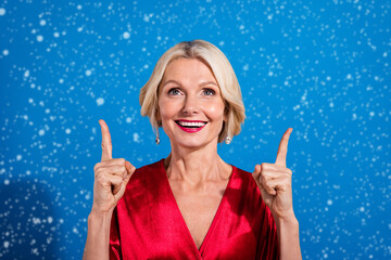 Wall Mural - Photo of adorable excited senior woman wear red shiny dress pointing up looking empty space isolated blue color background