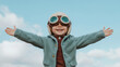 © NEXT-Ai - joyful child wearing aviator goggles and cozy jacket spreads their arms wide against clear blue sky, embodying sense of adventure and freedom