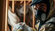 © ArpPSIqee - A close-up shot of an insulation installer in a protective suit and mask, holding insulation material and looking at the camera, with a wall cavity in the background