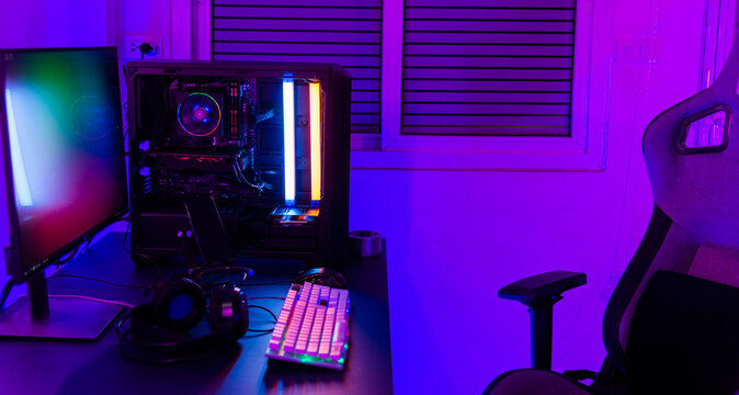 A computer setup with a purple light dark background, games transmission modern equipment, modern gaming PC on desk with keyboard mouse monitor, gamer work space concept
