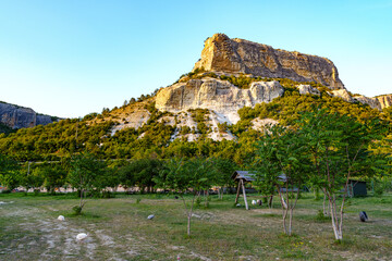 Wall Mural - a rugged cliff rises above a green landscape under a clear blue sky