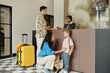 © DragonImages - Family with child standing at hotel reception desk checking in. Receptionist assisting them with smiling faces, luggage placed beside, creating atmosphere of a welcoming environment