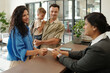 © DragonImages - Family arriving at reception desk, interacting with receptionist while holding child in arms. Receptionist handing over room key card with bright, welcoming demeanor