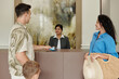 © DragonImages - Woman at reception counter smiling while family, consisting of a man, woman, and child, checking in during a vacation. Receptionist holding a room key card at modern hotel lobby
