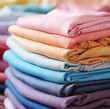 © C.Castilla - Pila de camisetas dobladas de colores.Primer plano de una prenda de moda con los colores del arco iris. Fondo de diferentes prendas de colores, muestra de tejido abstracto.