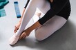 © Studio Marmellata - Close-up of a ballerina sitting on the studio floor wearing white tights and adjusting her pink ballet shoes, with soft lighting highlighting the details of her pose