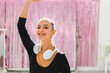 © Studio Marmellata - A ballerina with braces smiles brightly while wearing white headphones and a black top, exuding confidence and charm in a pink-decorated studio