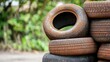© Jiraphiphat - rubber natural tires concept, A close-up of stacked old, rusty tires showcasing their worn texture against a blurred green background.