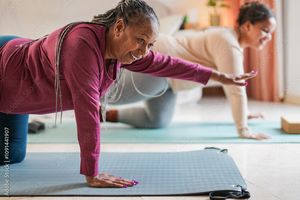 African mother and daughter doing yoga class together at home during ...