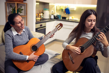 Wall Mural - Mother and daughter playing guitar at home. A mother teaches her daughter to play the guitar.