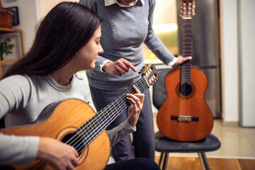 Wall Mural - Mother and daughter playing guitar at home. A mother teaches her daughter to play the guitar.