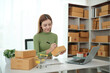 © Treerat - A woman is sitting at a desk with a laptop and a stack of boxes