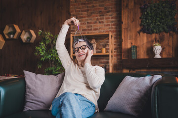 Happy elderly woman enjoying a relaxing weekend moment indoors, wearing casual attire. Joyful mature lady with glasses