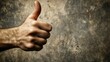 © Giovanni - Close-up view of a hand showing a thumbs up gesture against a textured gray background, emphasizing positivity and encouragement.