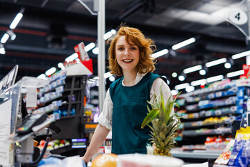 Wall Mural - Smiling cashier working at supermarket checkout counter