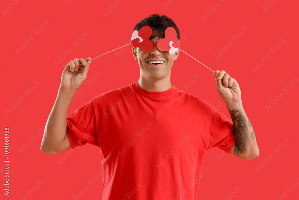 Young man with paper hearts on red background