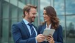 © natakot - Two business colleagues in formal attire are discussing work outdoors, using a tablet. The scene captures professionalism and teamwork in a modern business environment.