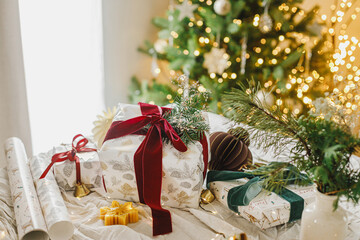 Wall Mural - Stylish christmas gift box with red ribbon, spruce branch and modern ornaments on background of decorated christmas tree. Merry Christmas and Happy Holidays. Modern Christmas present