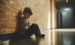 © Sergey - A young boy sits alone with a sad feeling at school near the wall. Offended child abandoned in the corridor and bent against a brick wall. Bullying, discrimination with copy space