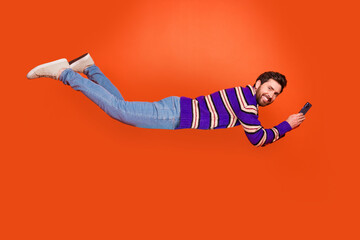 Aufkleber - Full body photo of attractive young man flying hold device dressed stylish striped purple clothes isolated on orange color background