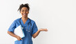 © Prostock-studio - Excited black female doctor in scrubs holding clipboard showing something on empty palm pointing with hand at free copy space, advertising poduct or clinic, posing isolated on white studio background