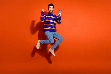 Poster - Full body photo of attractive young man mp hold device winning dressed stylish striped purple clothes isolated on orange color background