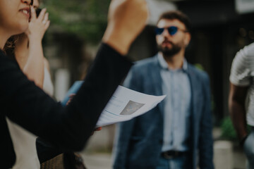 Canvas Print - Group of business professionals engaged in a lively discussion outdoors, sharing documents and ideas. The focus is on collaboration, teamwork, and strategic planning in a dynamic business environment.