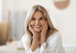 © Prostock-studio - Beautiful blonde middle aged woman smiling at camera, touching her face, attractive lady doing morning face care routine, white bathroom interior, blurred background, closeup portrait, copy space