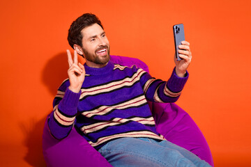 Poster - Photo of attractive young man sit beanbag v-sign selfie photo dressed stylish striped purple clothes isolated on orange color background