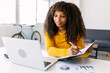 © Xavier Lorenzo - Young african american woman taking notes while attending on laptop video call. Business and education concept.