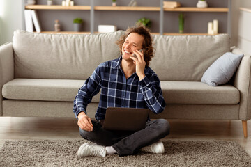 Poster - Mobile Communication. Cheerful Guy Talking On Smartphone Sitting With Laptop On Floor At Home, Working Remotely Online. Man Calling Speaking By Phone Having Pleasant Conversation