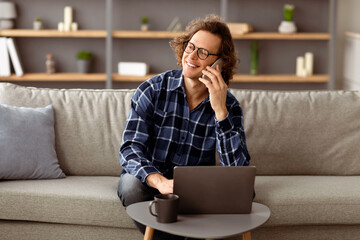 Poster - Communication. Cheerful Freelancer Man Talking On Cellphone Sitting With Laptop On Sofa At Home, Working Distantly Online. Long-Haired Guy Chatting On Smartphone Having Pleasant Phone Conversation