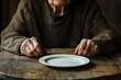 © Pramesti - Elderly Woman Hands Resting on Wooden Table Beside an Empty Plate, Depicting Solitude and Potential Poverty